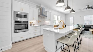 A modern kitchen with white cabinetry, stainless steel appliances, and a central island with bar stools. - Beach Please by Stay on 30a (Inlet Beach)