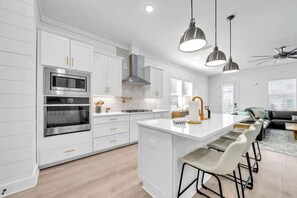 A modern kitchen with white cabinetry, stainless steel appliances, and a central island with bar stools. - Beach Please by Stay on 30a (Inlet Beach)