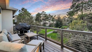 Une terrasse aménagée avec du mobilier d’extérieur, un barbecue et une vue sur un jardin paysager et des arbres.