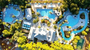 Luchtbeeld van een resort met diverse zwembaden, terrasjes en weelderige begroeiing.