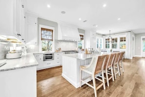 A spacious kitchen with white cabinetry, a large island, and a dining area with wooden chairs. - Tall Timber Retreat by Stay on 30a (Watercolor)