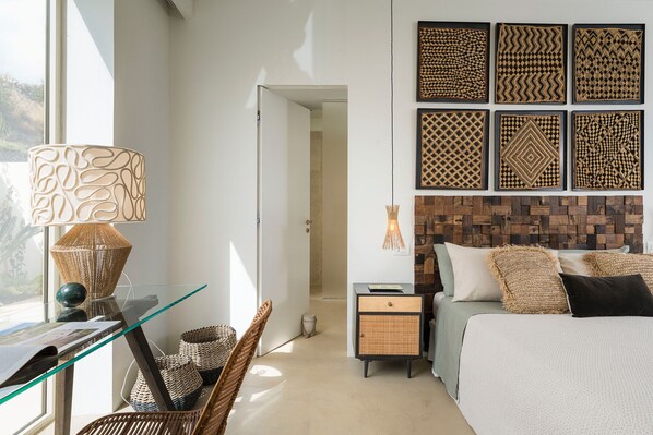 A modern bedroom with a glass desk, wicker chair, and a bed with a wooden headboard.