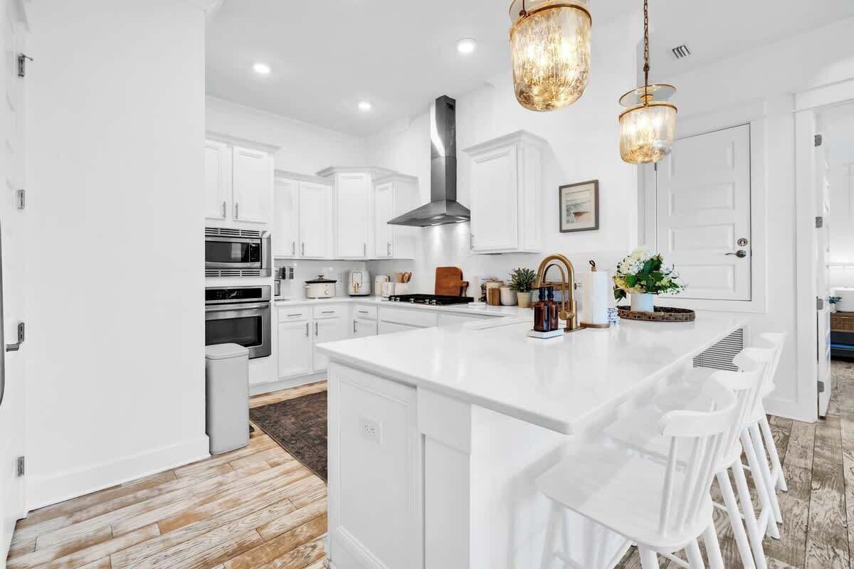 A modern kitchen with white cabinetry, a central island, bar stools, and pendant lighting.