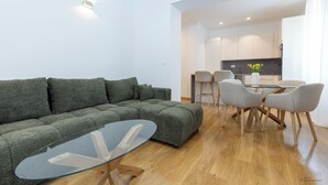 Ein modernes Wohnzimmer mit einem grünen Sofa, einem Glastisch und einem Essbereich mit einem Tisch aus Glas und vier Stühlen.
