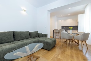 Un salon moderne avec un canapé vert, une table basse en verre et un coin repas comprenant une table en verre et quatre chaises.