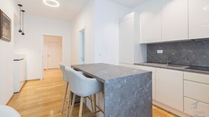 Eine moderne Küche mit weißen Schränken, einer Marmorarbeitsplatte und einer Bar mit zwei Barhocker.