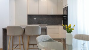 Eine moderne Küche mit Marmorarbeitsplatte, Edelstahlgeräten und einem Glastisch mit Barhocker.