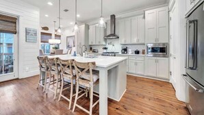 Una cocina moderna con armarios blancos, una isla grande con taburetes de bar, electrodomésticos de acero inoxidable e iluminación colgante.