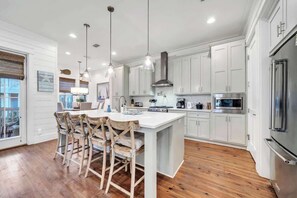 A modern kitchen with white cabinets, a large island with bar stools, stainless steel appliances, and pendant lighting. - Best Kept Seacrest by Stay on 30a (Seacrest Beach)
