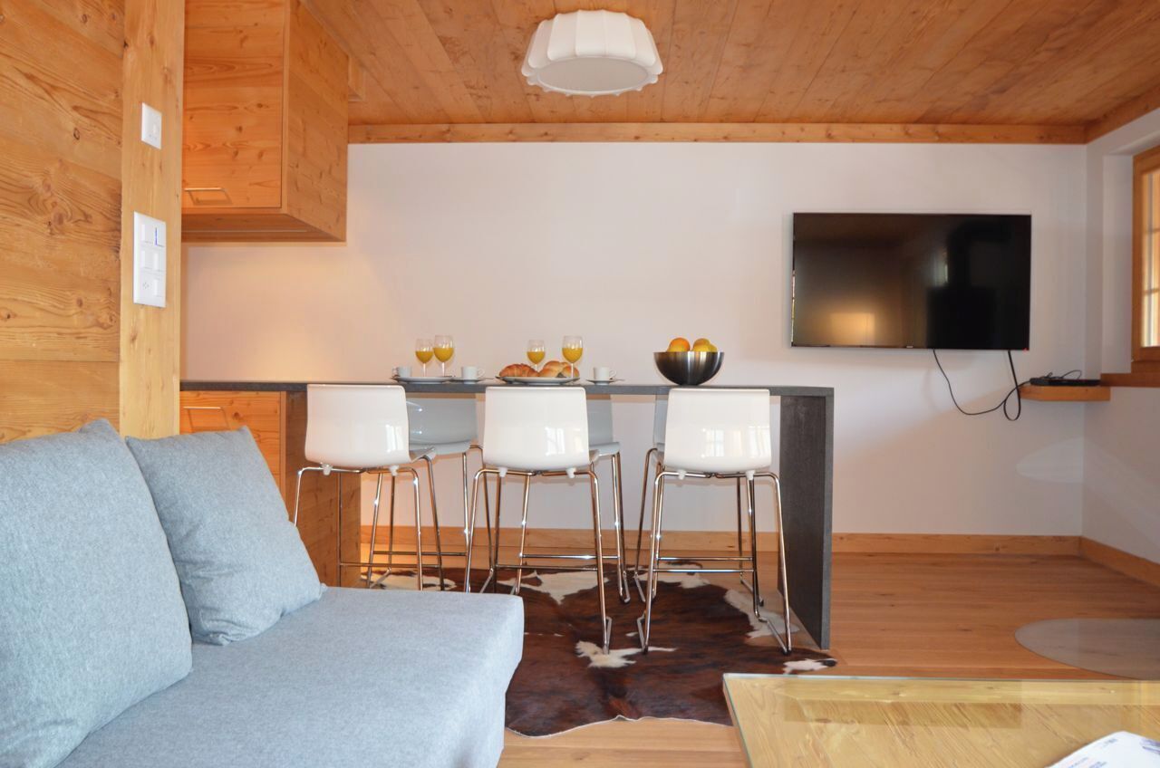 L’intérieur chaleureux d’un chalet avec un plafond en bois, un téléviseur à écran plat fixé au mur, un coin repas avec une table et des chaises, et un canapé.