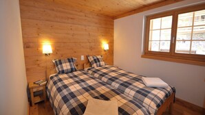 Une chambre avec un plafond en bois, deux tables de chevet avec des lampes, un lit recouvert d’une couverture à carreaux et une fenêtre donnant sur l’extérieur.