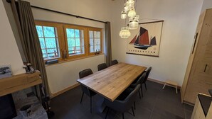 Zona pranzo con tavolo e sedie in legno, finestra con tende, quadro di una barca a vela appeso al muro e lampadario.