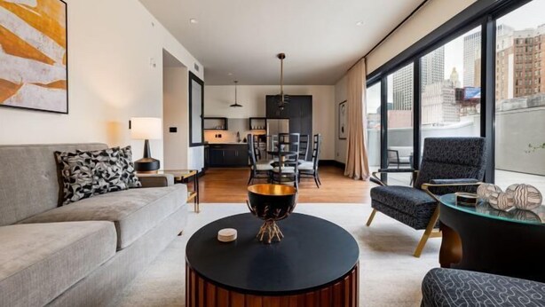 A modern living room with a round coffee table, a sofa, and a dining area with chairs. - 3BR Lavish Penthouse + Canal St Private Patio The Mayfair (New Orleans)