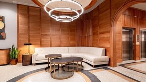 A lobby with a white sofa, round tables, a modern light fixture, wooden paneling, and an elevator. - 3BR Lavish Penthouse + Canal St Private Patio The Mayfair (New Orleans)