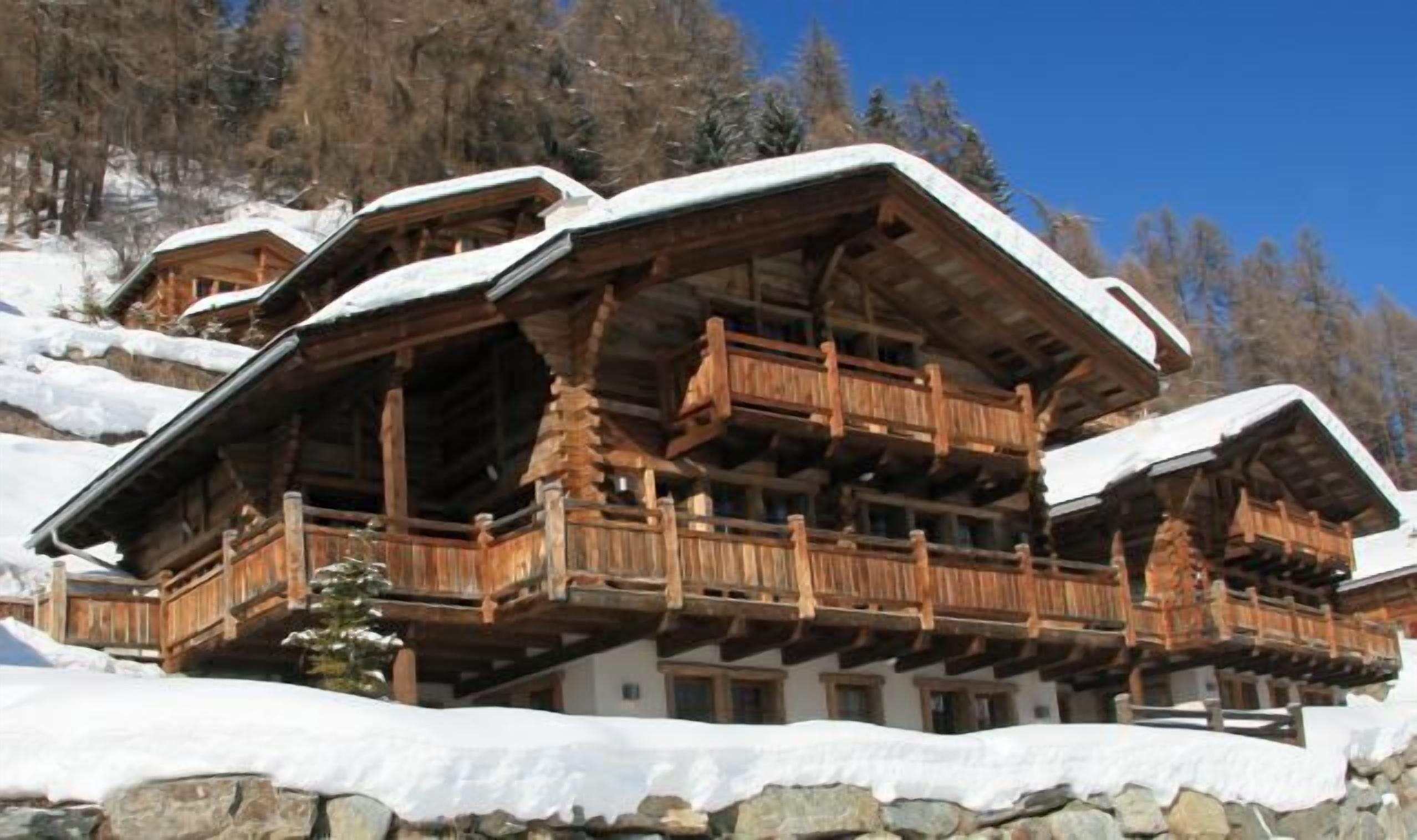 A traditional wooden chalet with a balcony, set in a snowy mountainous area.