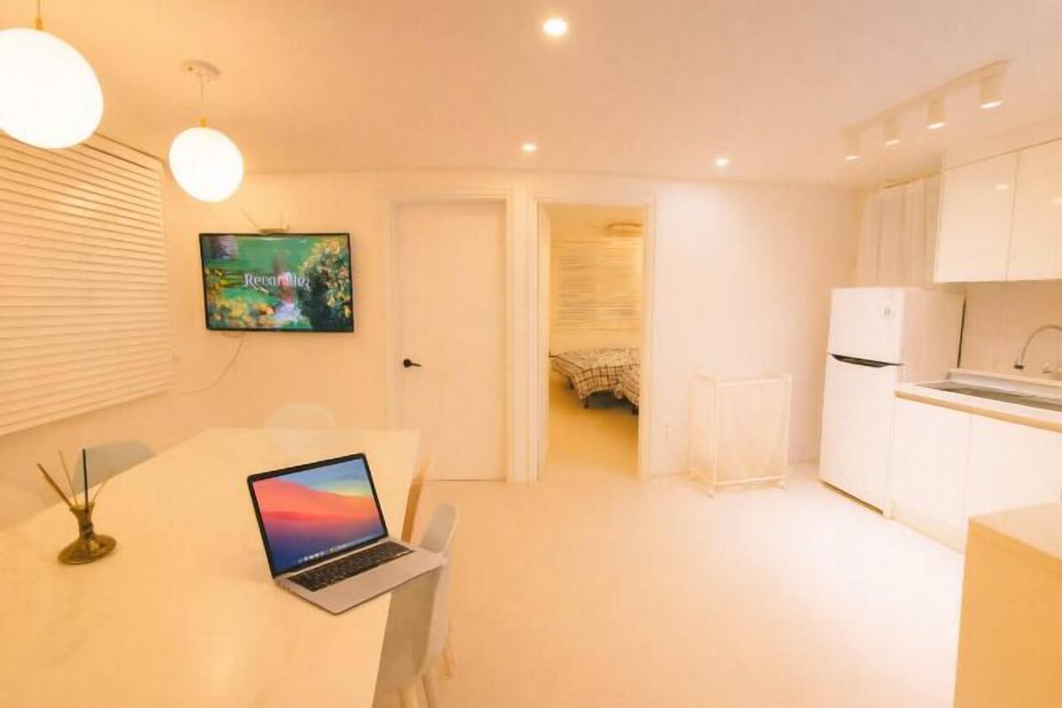 Un angolo cottura compatto con un portatile su un tavolo, una TV a parete e un letto sullo sfondo.