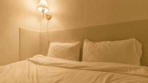 En seng med hvide sengetøj, en vægmonteret lampe og en ensfarvet væg.