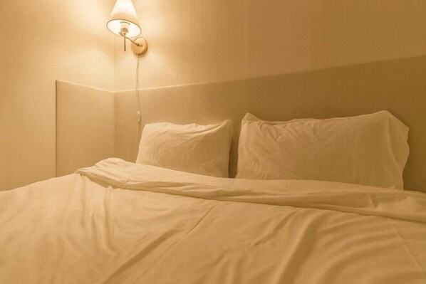 Un letto con biancheria bianca, un lampadario a parete e una parete spoglia.