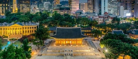 A traditional building with a tiled roof and a courtyard surrounded by trees, set against a modern city skyline.