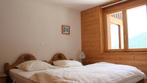 Ein Schlafzimmer einer Holzhütte mit einem Einzelbett, einem Nachttisch, einem kleinen Beistelltisch und einem Fenster mit Holzläden.