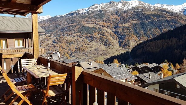 A wooden deck with a table and chairs overlooking a mountainous landscape with snow-capped peaks and autumn-colored trees. - 3-room apartment for 6 persons : living room - kitchen with dishwasher and microwave - 1 room with 1 (Grimentz)