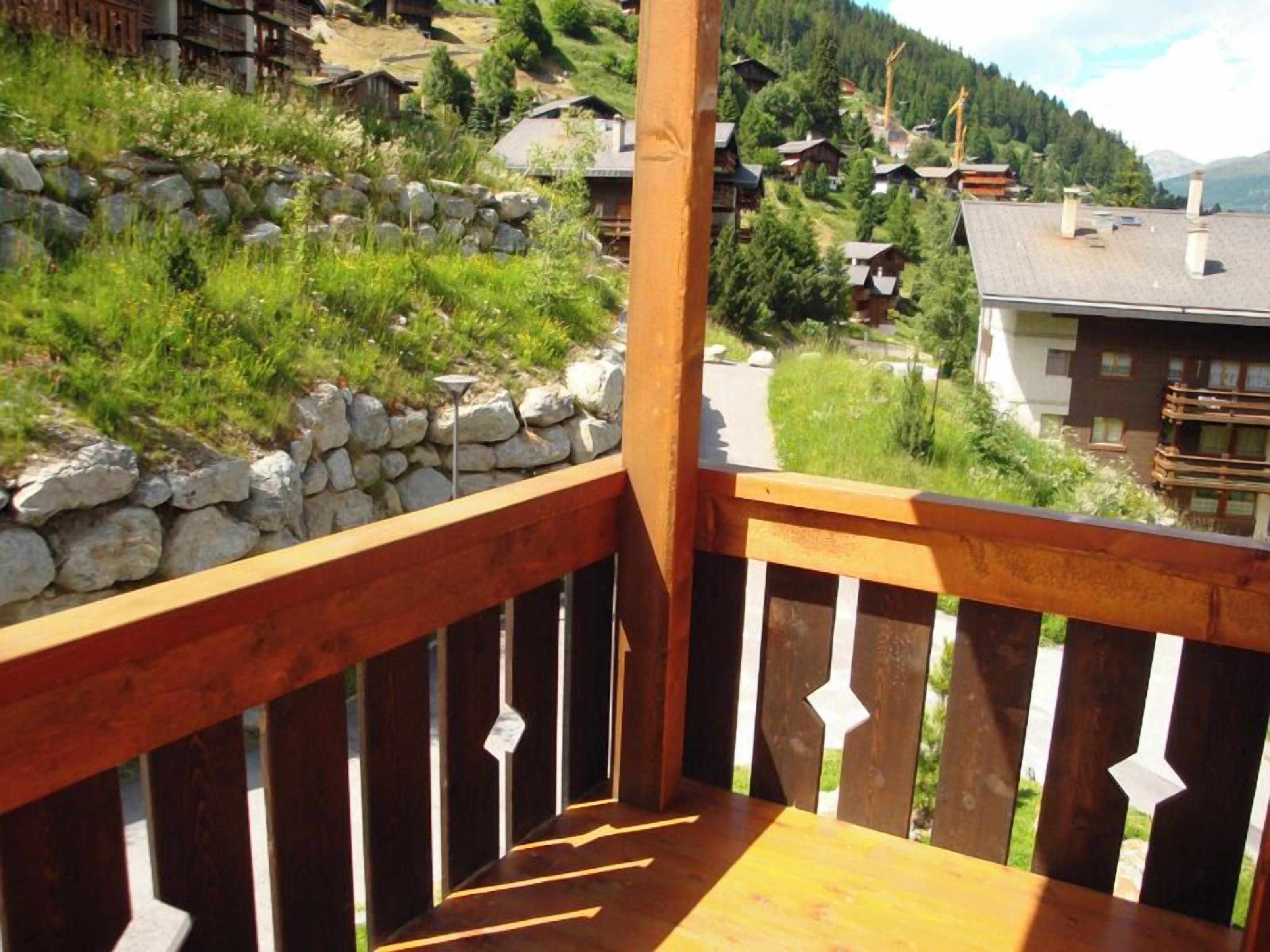 Ein Holzbalkon mit einer Steinmauer und Blick auf ein Dorf mit Häusern und Bäumen.