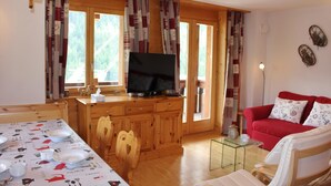 A cozy living room with a red sofa, wooden dining table with white tablecloth, and a TV on a wooden cabinet. - 3-room apartment for 6 persons : living room - kitchen with dishwasher and microwave - 1 room with 1 (Grimentz)