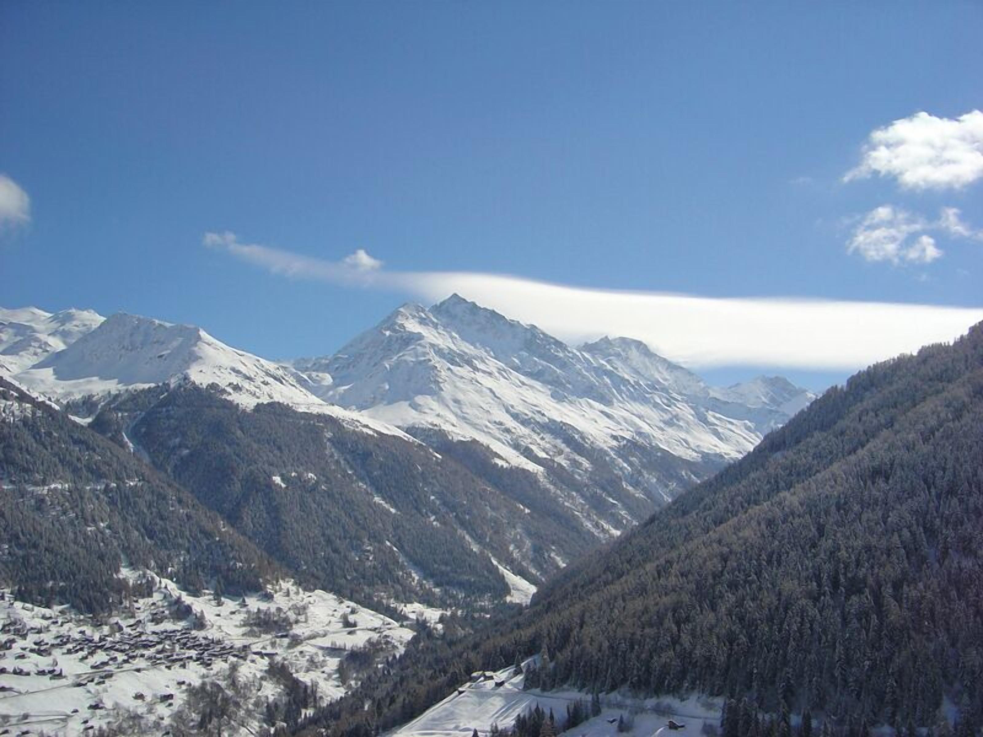 A mountainous landscape with snow-covered peaks and dense forests.