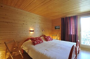 Ein Schlafzimmer mit Holzwänden, einem Bett, Kissen, einem Sessel und einem Fenster mit Vorhängen.