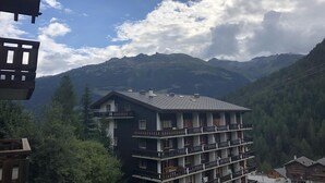 Un hotel a più piani con balconi, sullo sfondo montagne e un cielo parzialmente nuvoloso.