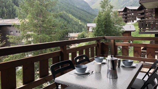 Un balcone con un tavolo apparecchiato per due, con vista su un paesaggio montuoso.