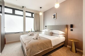 A neatly made bed with white linens and a beige throw blanket, a bedside table with a gold finish, and a window with curtains. - Le White by Sweett (Paris)
