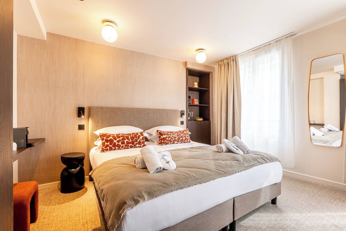 A modern hotel room with a large bed, a small side table, a built-in shelf, and a large mirror.