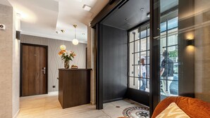 A modern hotel lobby with a reception desk, a patterned rug, and a large window with a view of the street. - Le White by Sweett (Paris)