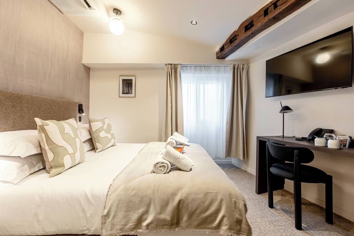 A hotel room with a bed, a desk, a chair, a TV, and a window with curtains.