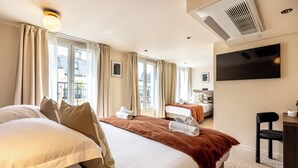 A hotel room with two beds, a desk, a chair, a TV, and an air conditioning unit. - Le White by Sweett (Paris)