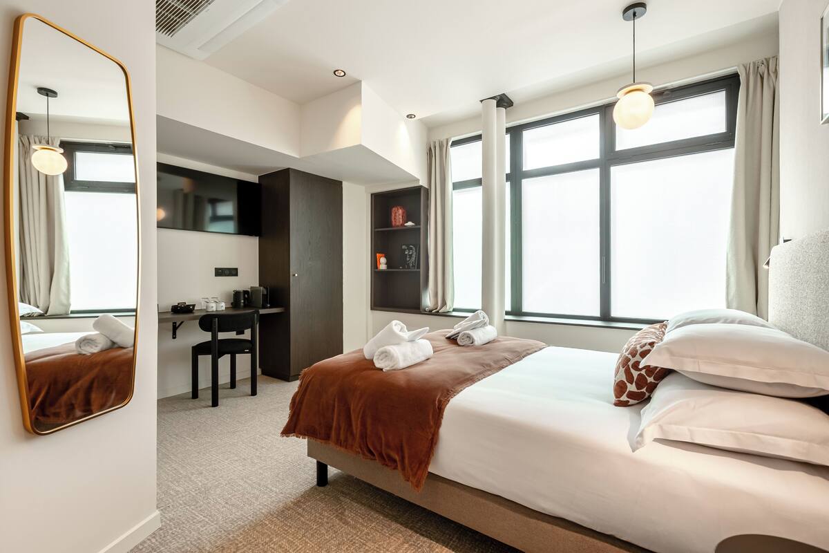A hotel room with a large bed, a desk, a chair, and a wardrobe.