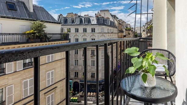 A balcony with a view of Parisian buildings, a potted plant, and a chair. - Le White by Sweett (Paris)
