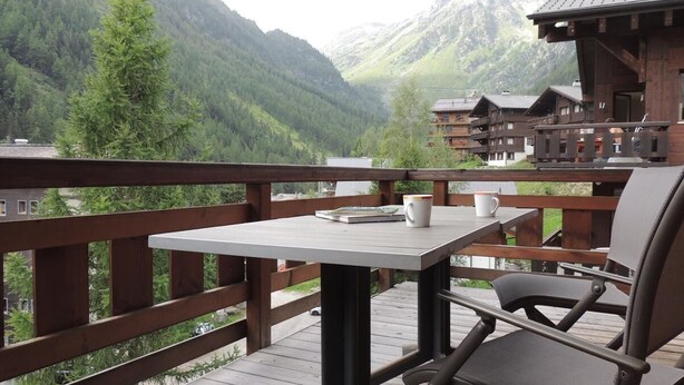 Terraza de madera con mesa y sillas que da a un paisaje montañoso.