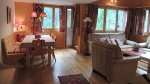 Un salón acogedor con suelo de madera, un sofá, una mesa de comedor con sillas y una ventana con cortinas.
