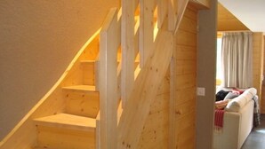 Una escalera de madera que conduce a una sala de estar con un sofá y un ventanal con cortinas.