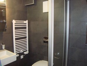 Un baño con un lavamanos blanco, toallero, inodoro y zona de ducha.