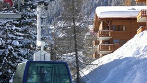Un chalet de madera con balcón, rodeado de árboles cubiertos de nieve y un telesilla al fondo.