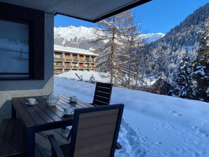 A wooden table with a chair and a window overlooking a snow-covered mountain and a building with balconies. - Very comfortable 4-room apartment for 6 persons : Living room - kitchen with dishwasher, Microwave a (Grimentz)