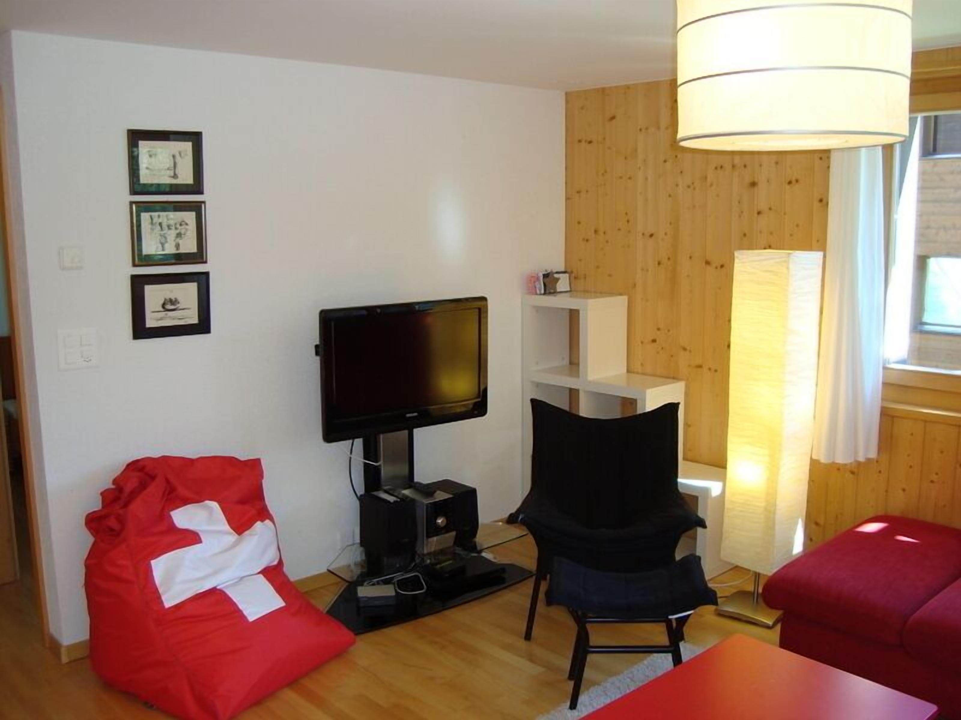 Ein Wohnzimmer mit einem Flachbildfernseher, einem roten Sitzsack, einem schwarzen Sessel und einem roten Sofa.