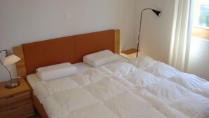 Un letto rifatto con biancheria bianca, una testiera in legno, una lampada da comodino e un comodino con un cassetto.