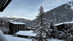 Ein schneebedecktes Bergresort mit mehreren Gebäuden, darunter eine Lodge mit Balkonen und einer Seilbahn im Hintergrund.