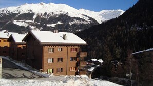 Ein mehrstöckiges Gebäude mit schneebedecktem Dach, vor einer Kulisse aus verschneiten Bergen und dichtem Wald.