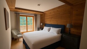 Un dormitorio con una cama grande, paredes de madera, una ventana con cortinas, una silla y mesitas de noche.