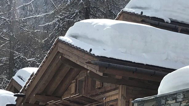 Una cabaña de madera con fachada de piedra, un balcón y alrededores cubiertos de nieve.